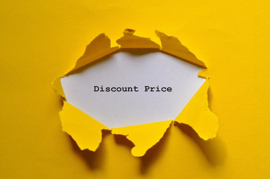 A piece of vibrant yellow paper with torn edges has been ripped open from a flat, bright yellow background, revealing a white paper insert underneath. The white paper displays the text 'Discount Price' in a black, typewriter-style font. The torn edges cast subtle shadows, emphasizing the layered effect. The overall scene suggests a focus on savings or special offers, which may be associated with house removals or relocation services offered by Man With a Van Aldersbrook, as indicated by the context of the webpage about avoiding hidden fees in moving costs. The setup is clean and minimal, with clear visibility of the torn paper, the text, and the contrasting background, highlighting the concept of uncovering deals or discounts related to furniture transport or home relocation services.
